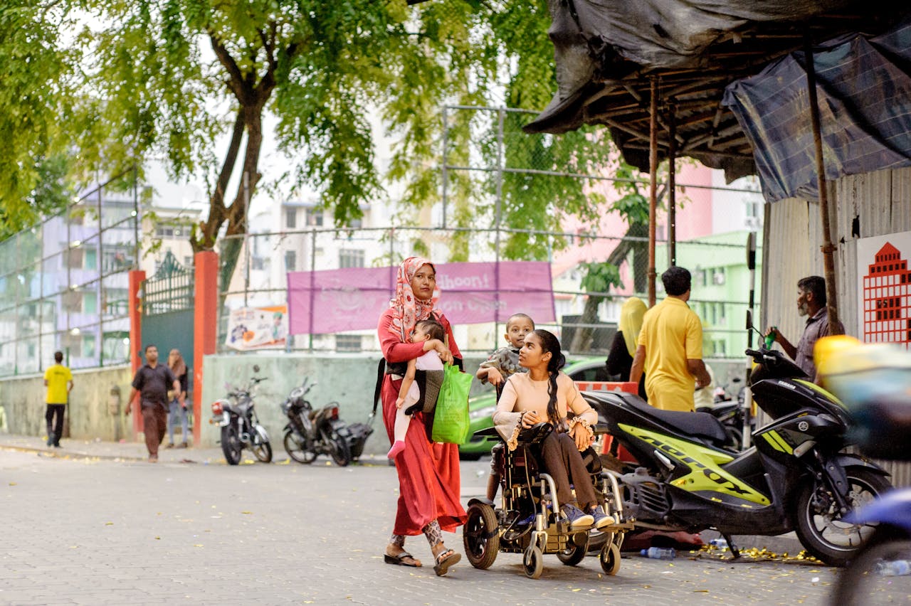 about-01 Two women, one in a wheelchair, navigate a lively urban street, capturing daily life and accessibility.