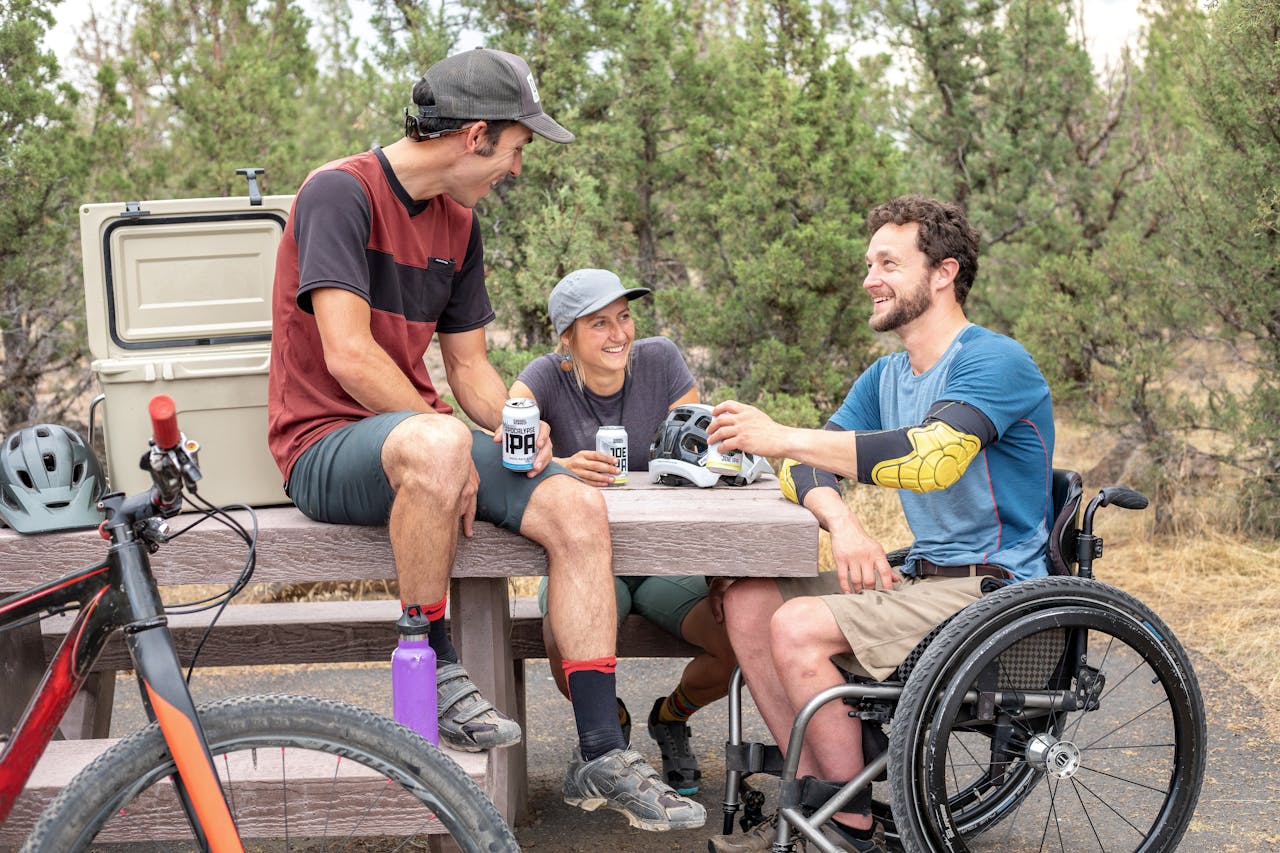 about-04 Group of friends having fun outdoors, chatting and enjoying drinks by a picnic table.