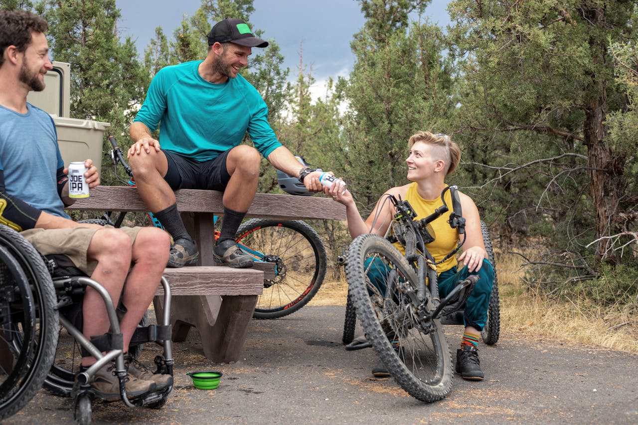services-03 Friends enjoying a relaxing outdoor activity with hand bikes and drinks in a park setting.