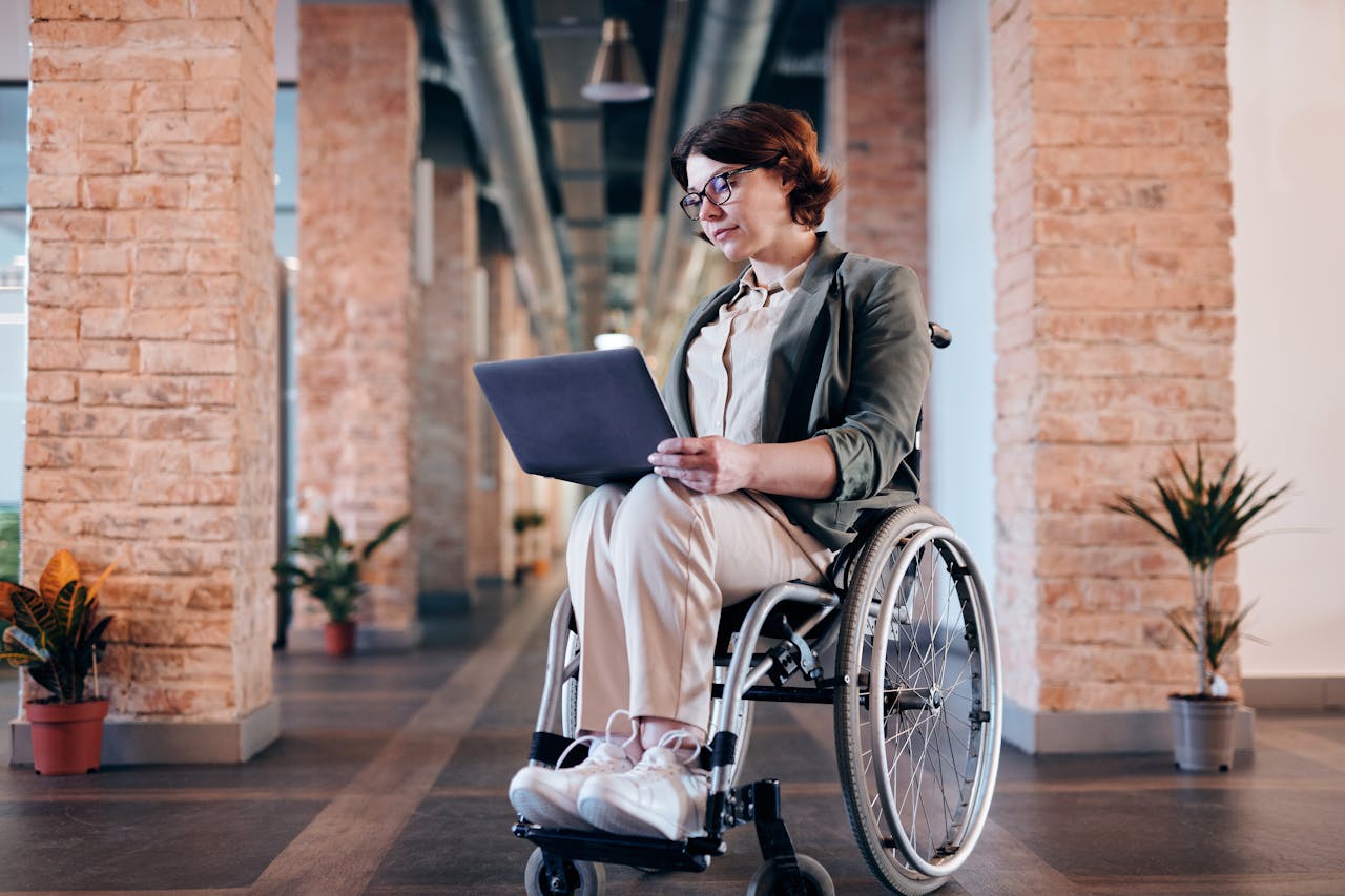 services-01 Businesswoman in wheelchair using laptop indoors, showcasing modern remote work setup.