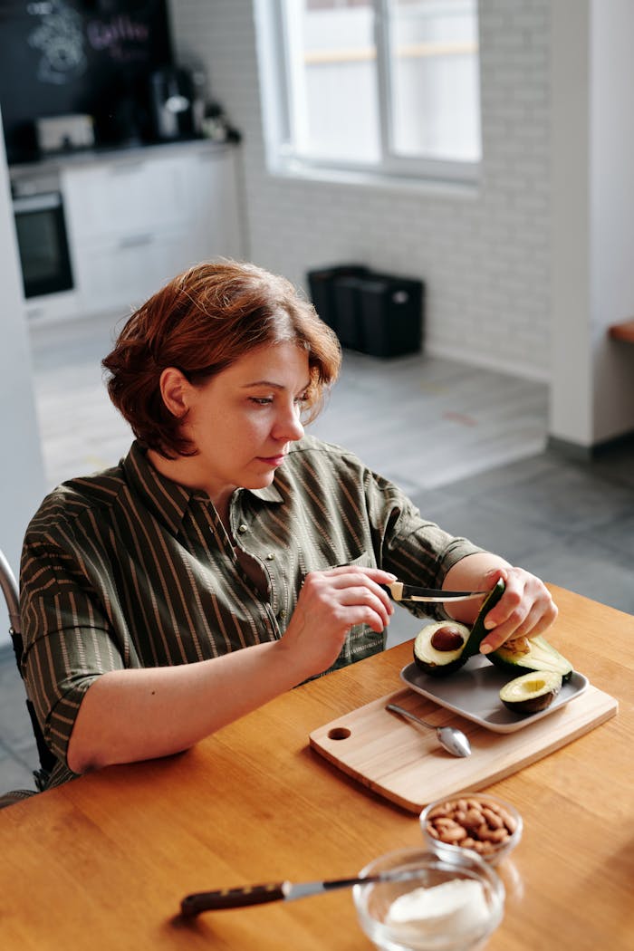 about-07 Woman cutting avocado at home kitchen table, enjoying a healthy meal preparation.