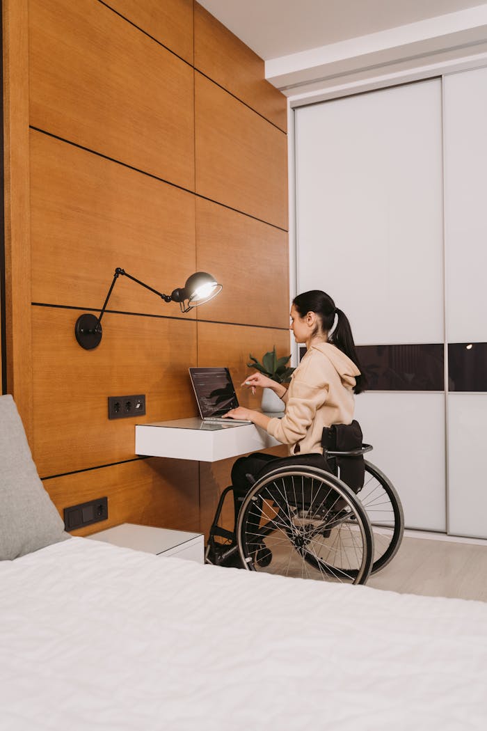 about-05 Woman in a wheelchair working on a laptop in a modern bedroom setting.